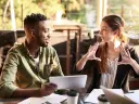 Two people sitting at a table consulting on a tablet.